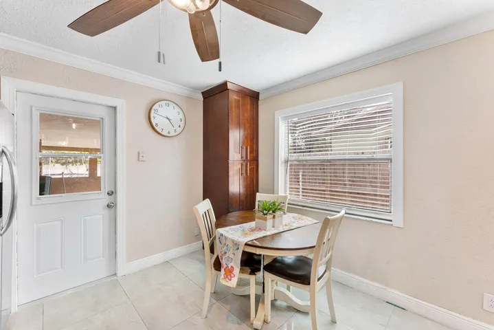 Recessed ceiling with an overhead fan light fixture, tile flooring, built-in wooden cabinetry, white paneled door with glass insert, and a window with horizontal blinds