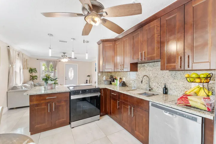 Modern kitchen featuring wood cabinetry, light-toned countertops, tile flooring, stainless steel appliances, and a central island with an integrated range