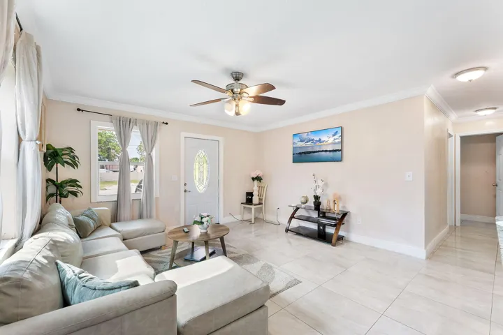 Spacious living area featuring light-toned walls, crown molding, and large format tile flooring