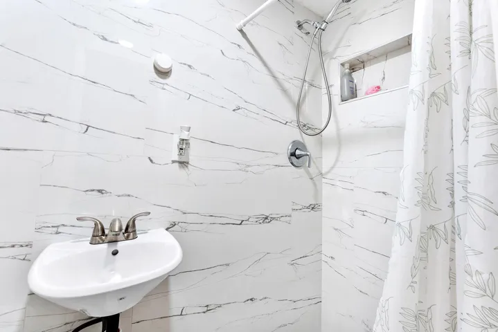 White tiled shower with a built-in niche, chrome shower fixtures, and an adjacent wall-mounted sink with brushed nickel faucet