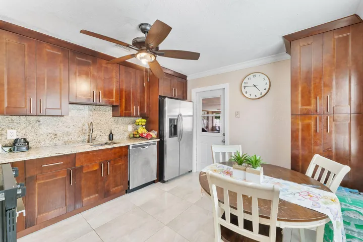 Kitchen featuring extensive wood cabinetry, granite countertops, tile flooring, stainless steel appliances, and a ceiling fan with integrated lighting