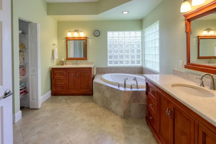 Spacious primary bathroom featuring dual vanities, a Roman soaking tub, separate walk-in shower, and abundant natural light.