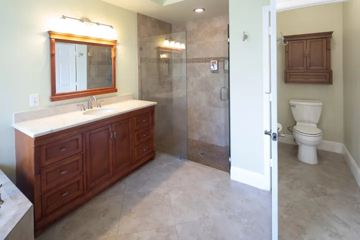 Alternate view of the primary bathroom highlighting the dual-sink vanity, walk-in shower, and private water closet.
