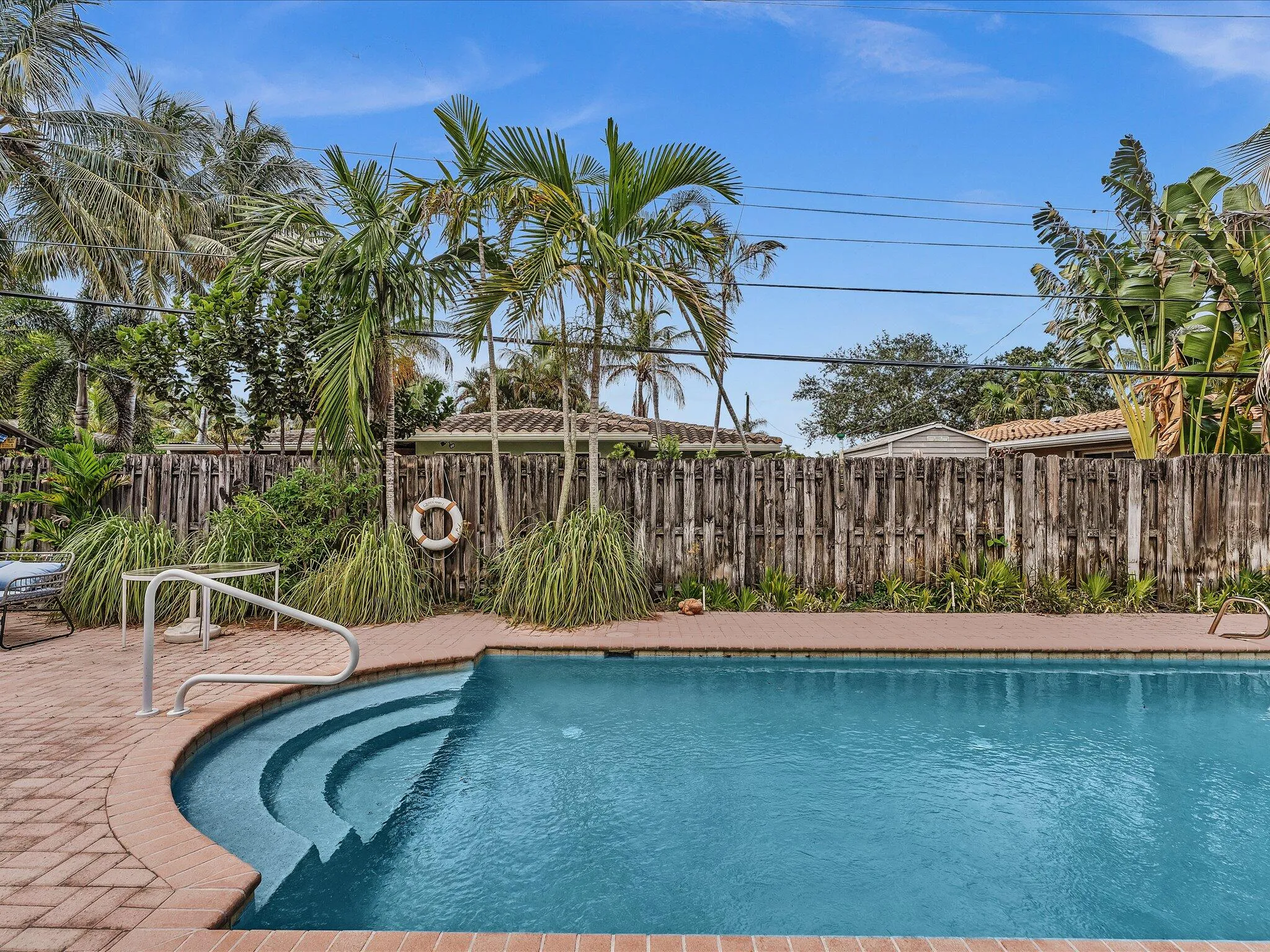Private pool with integrated steps, surrounded by brick paver decking and mature tropical landscaping
