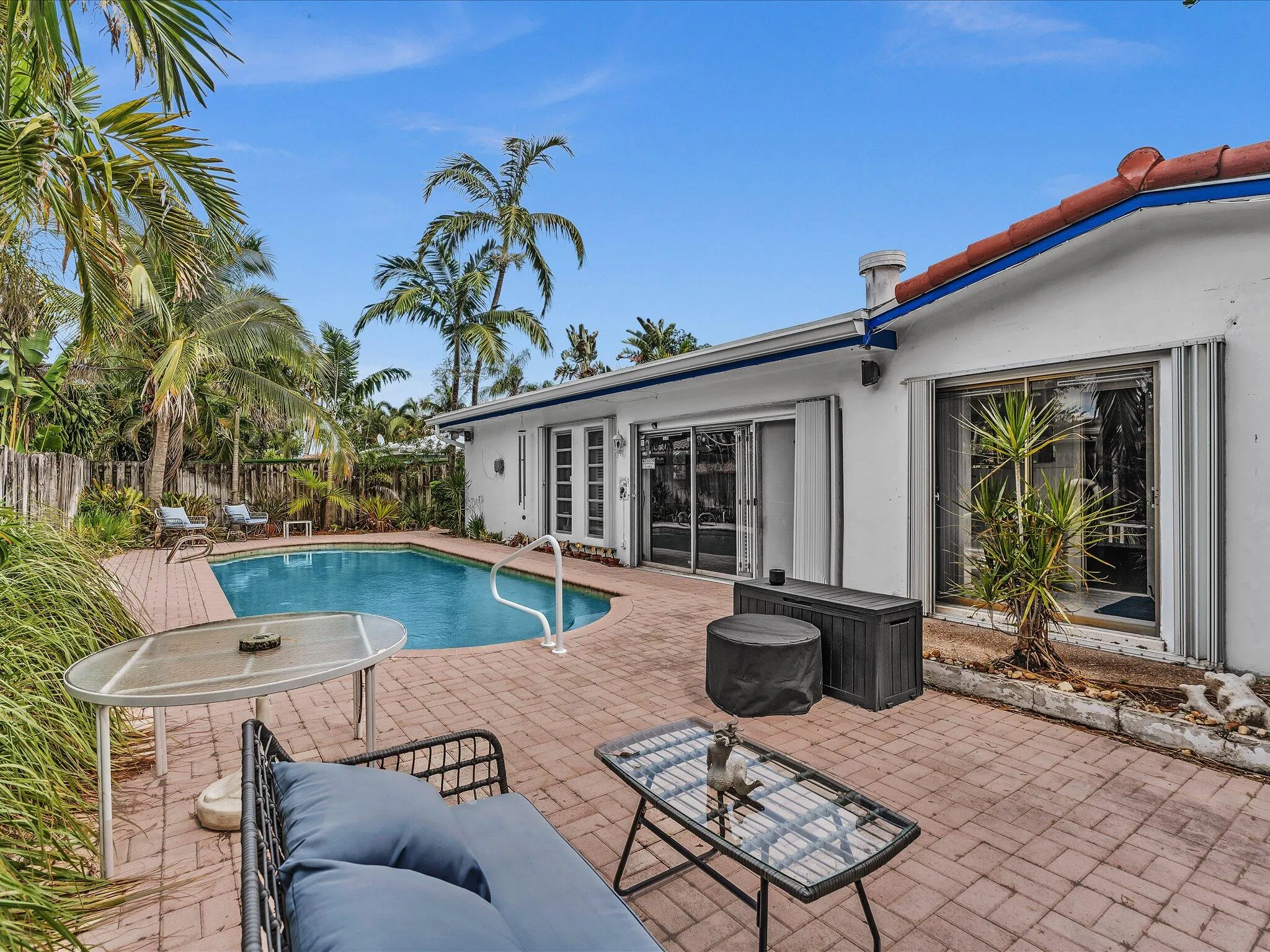 Outdoor pool area featuring a freeform swimming pool, extensive red brick paver patio, and mature palm trees