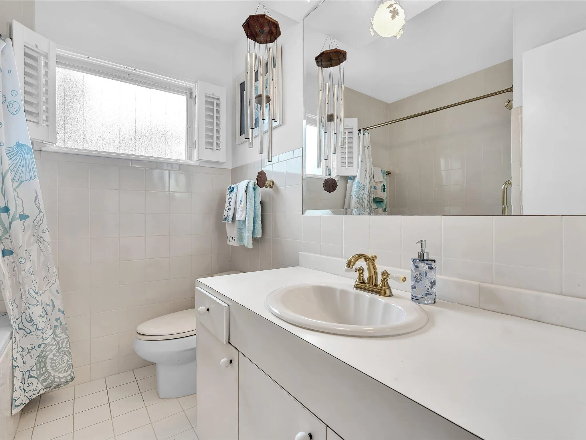 Bathroom vanity featuring an integrated sink with a brass-finish faucet, a large wall-mounted mirror, and white cabinetry