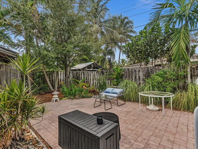 Brick paver patio surrounded by lush, mature landscaping and a wooden fence