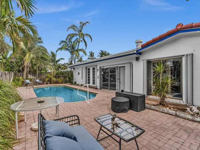 Outdoor pool area featuring a freeform swimming pool, extensive red brick paver patio, and mature palm trees