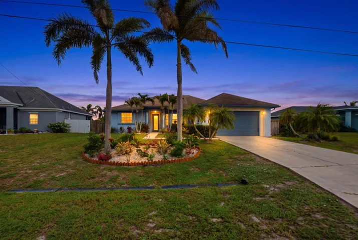 Single-story residence featuring a two-car garage, mature palm trees, and a landscaped front garden with a decorative border