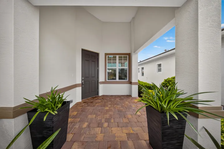 Covered entryway featuring a paneled front door, an exterior window with grid patterns, and a multi-tone paver floor