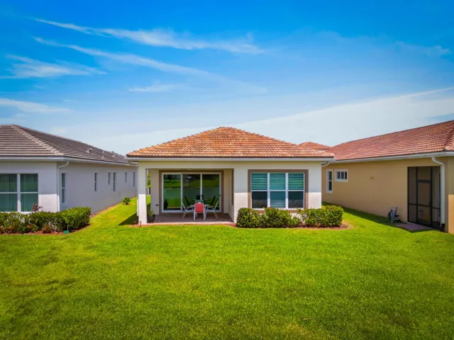 Expansive rear yard featuring a manicured lawn, covered patio, sliding glass doors, mature landscaping, and a tile roof