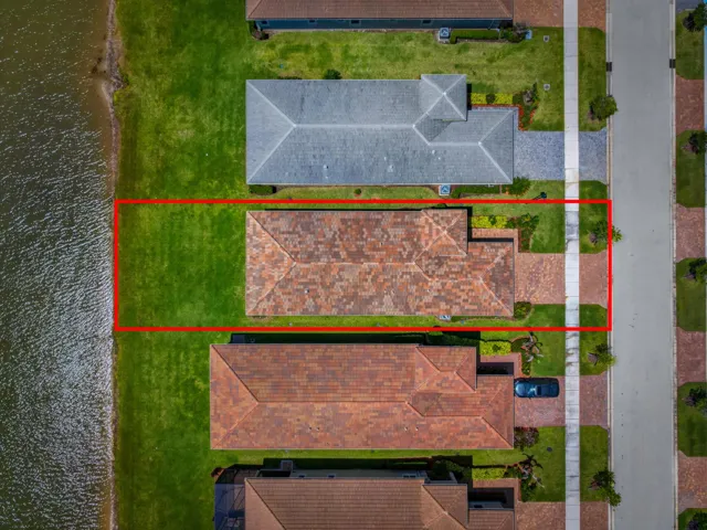 Property featuring a tile roof, a substantial grassy area bordering a body of water, and a paved driveway