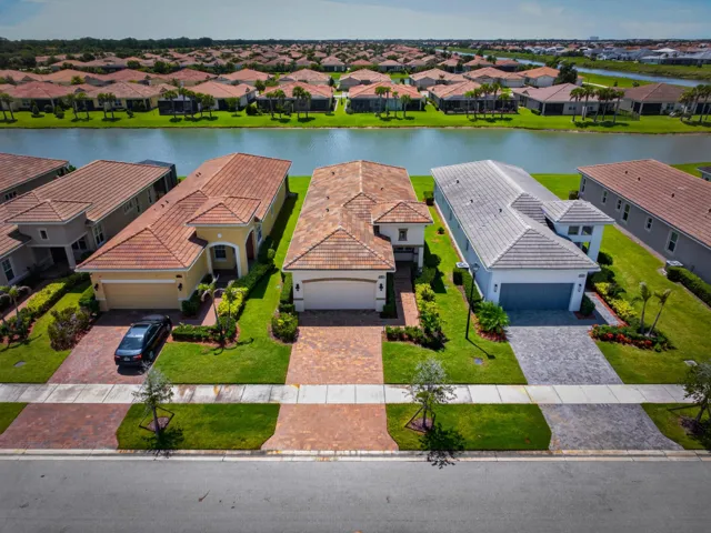 Waterfront residential community featuring a paved street, landscaped front yards with mature trees, and a direct water canal