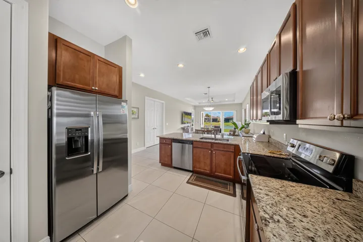 Kitchen featuring stainless steel appliances, granite countertops, wood cabinetry, recessed lighting, and tile flooring