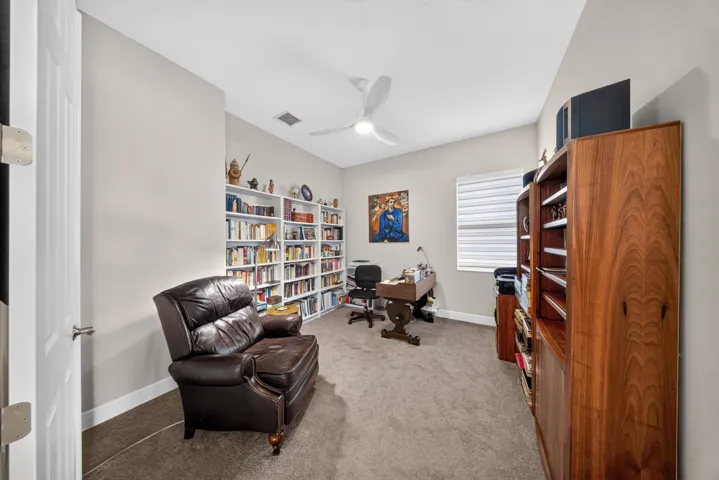 Carpeted room featuring a ceiling fan, a window with horizontal blinds, and a built-in white bookshelf