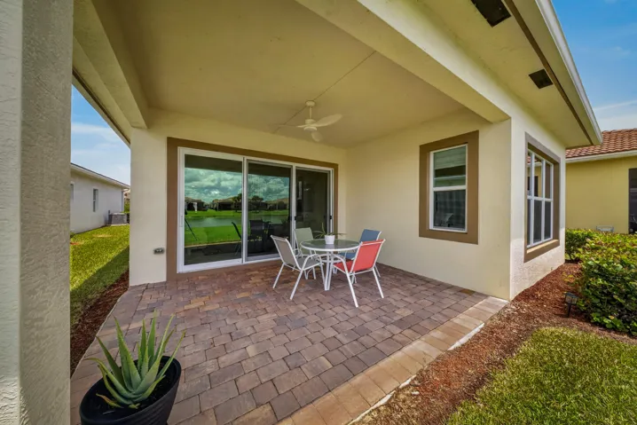 Covered paver patio featuring a ceiling fan, sliding glass doors, and multiple windows