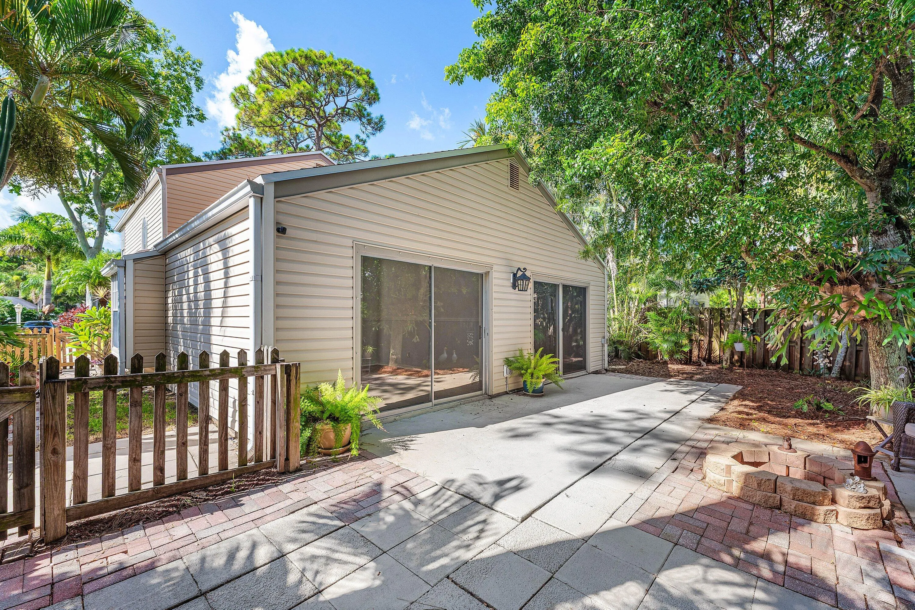 Expansive outdoor patio featuring paver and concrete surfaces, a built-in brick fire pit, and mature trees providing natural shading