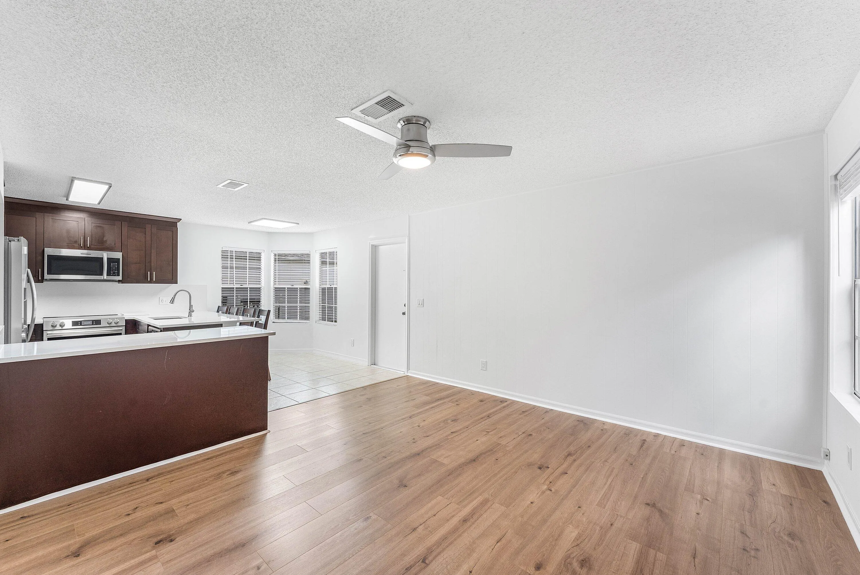 Open-concept living space featuring wood-finish flooring, a contemporary ceiling fan, and abundant natural light from multiple windows