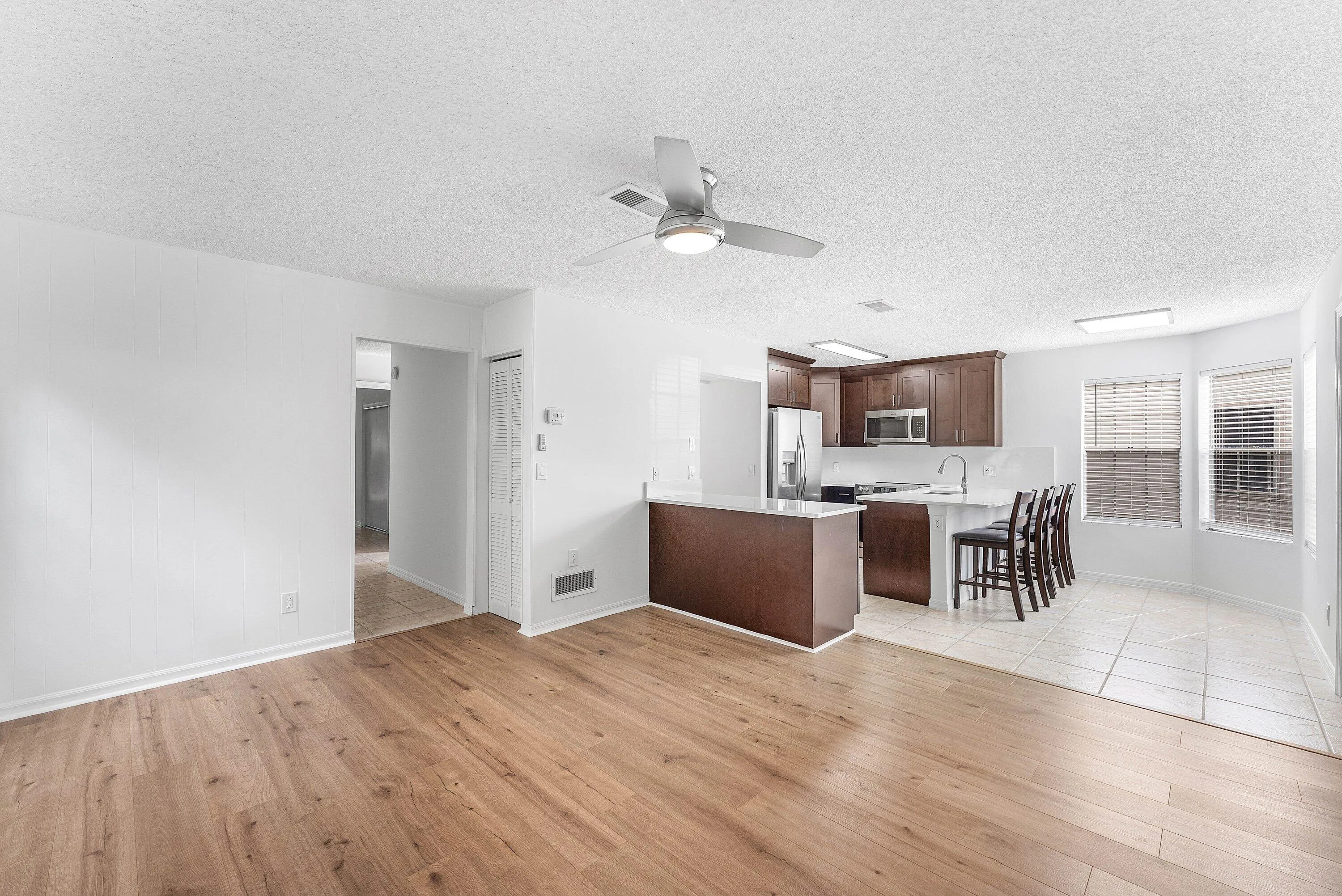 Open-concept living area featuring wood-finish flooring, a contemporary ceiling fan with integrated lighting, and white walls