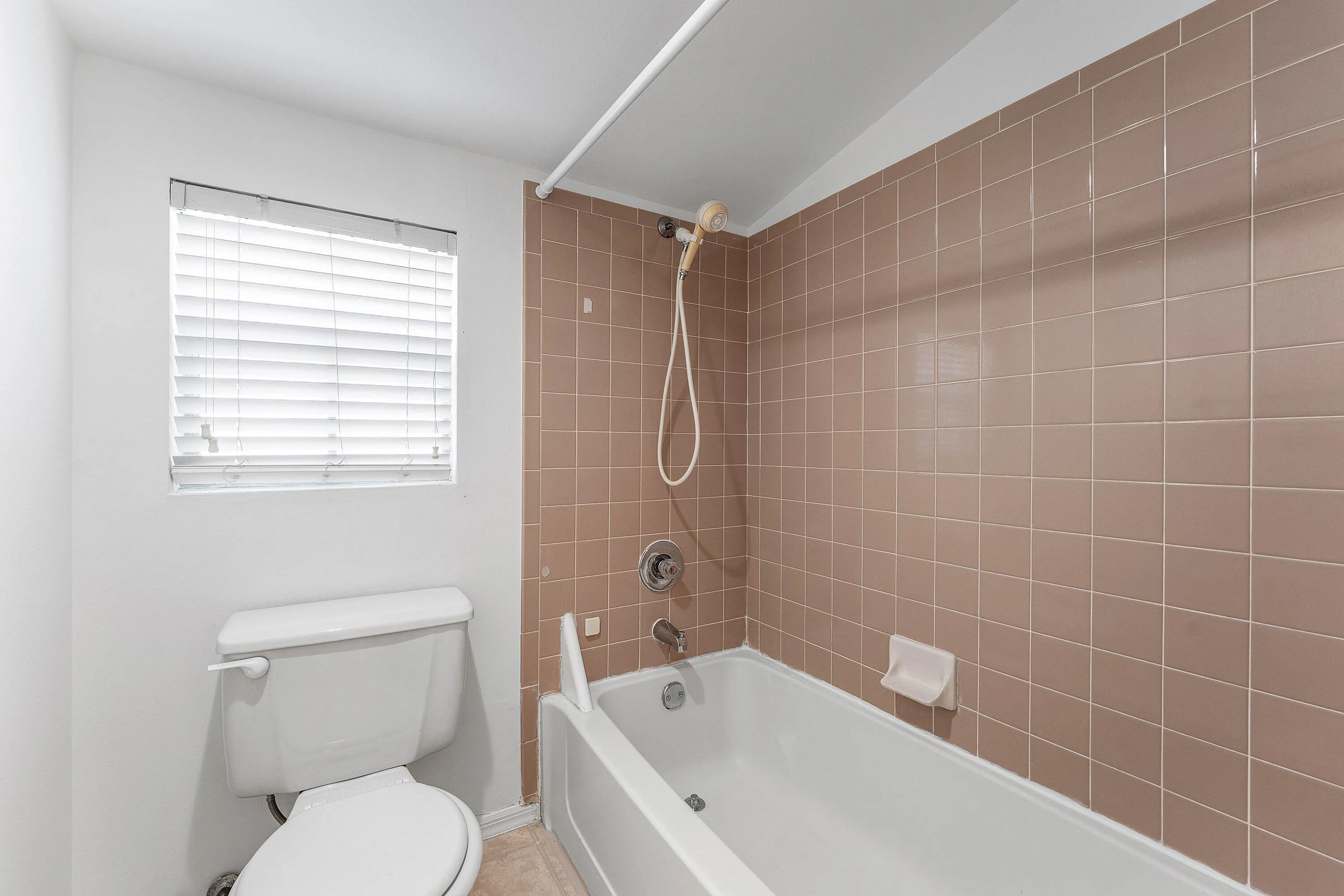 Bathroom with a bathtub and shower combination, featuring brown square wall tiles and a white toilet