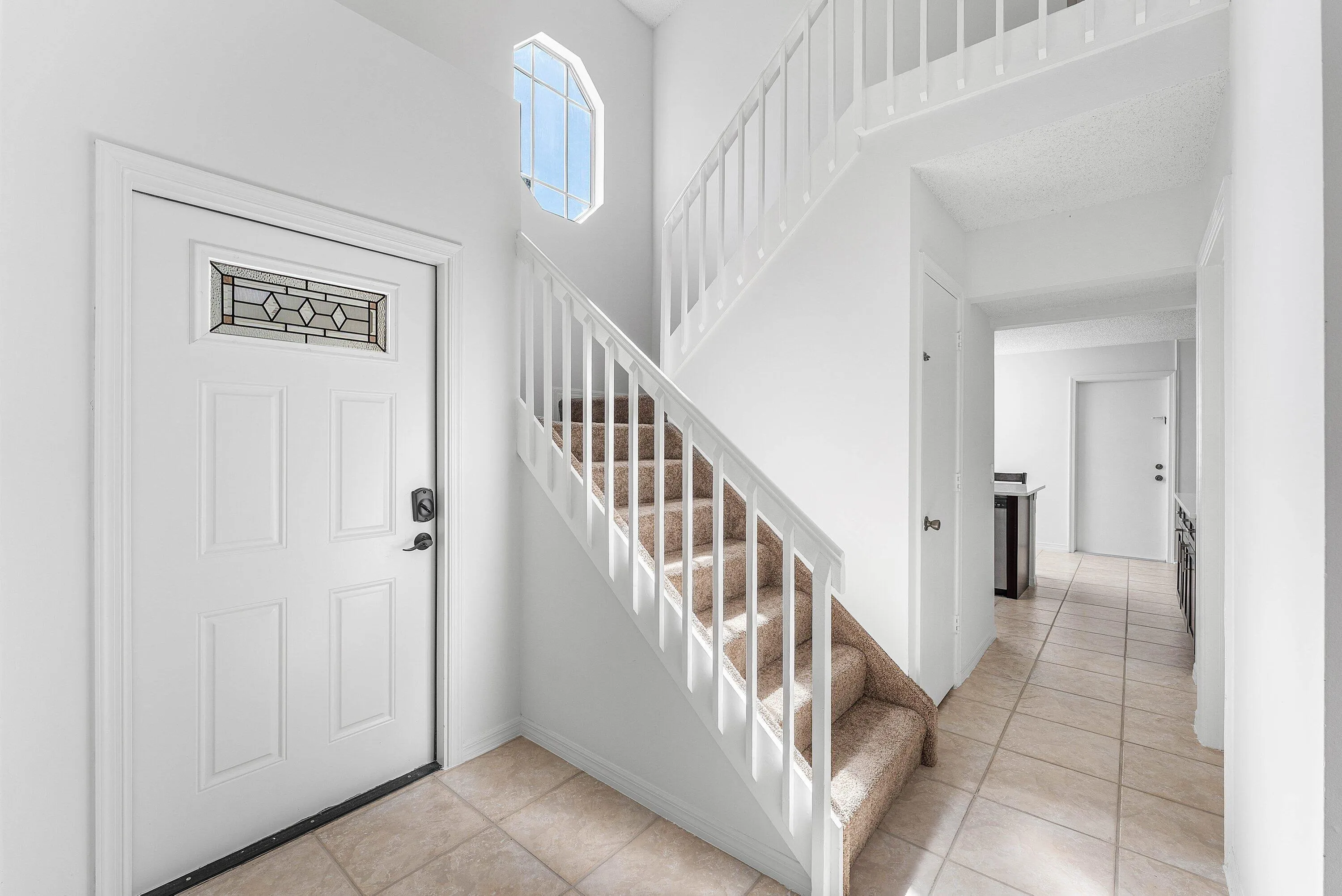 Entryway featuring a white paneled door with decorative glass insert, an arched window, a carpeted staircase with white railings, and tile flooring extending through a hallway
