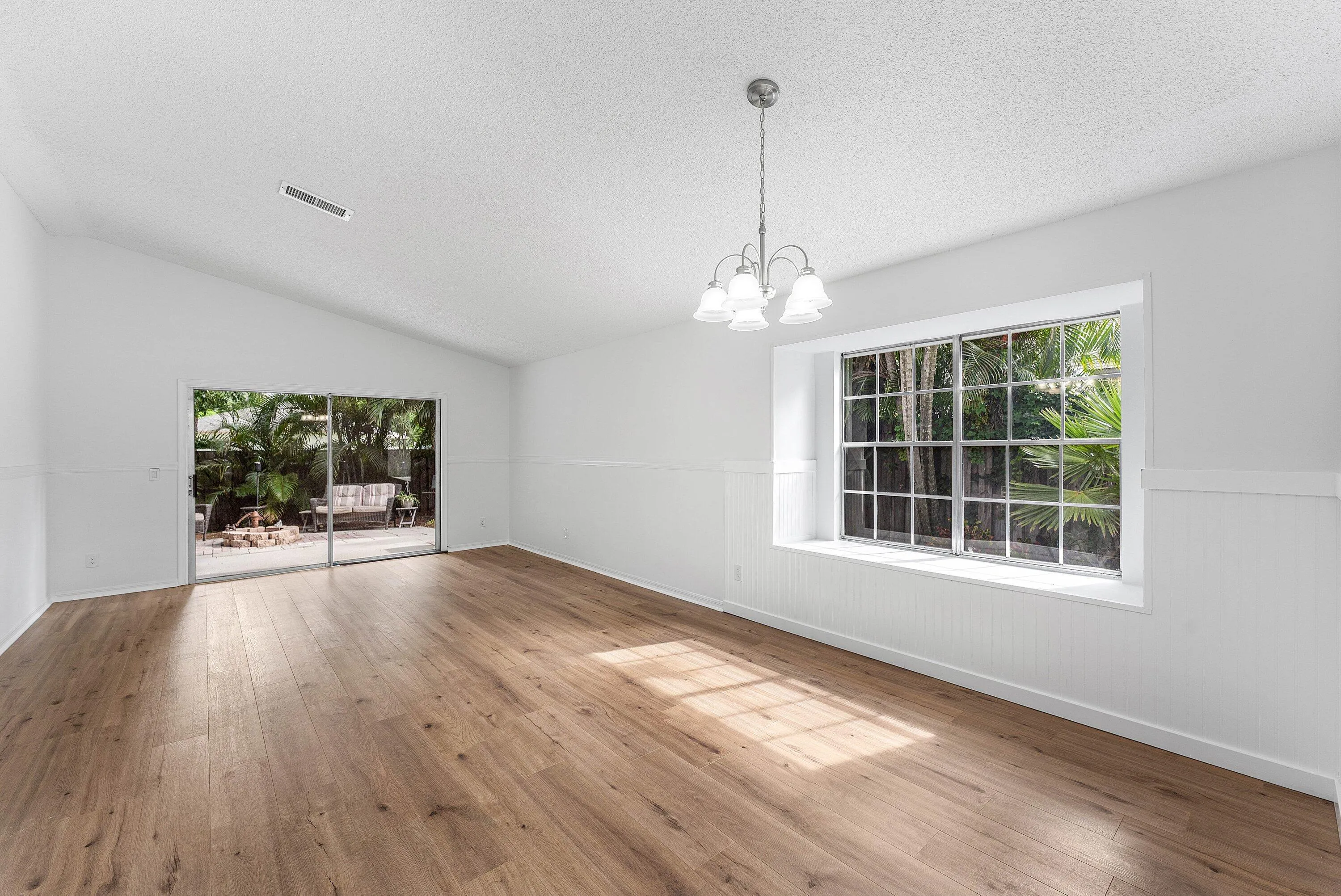 Spacious room featuring wood-finish flooring, a vaulted ceiling, and white walls with wainscoting