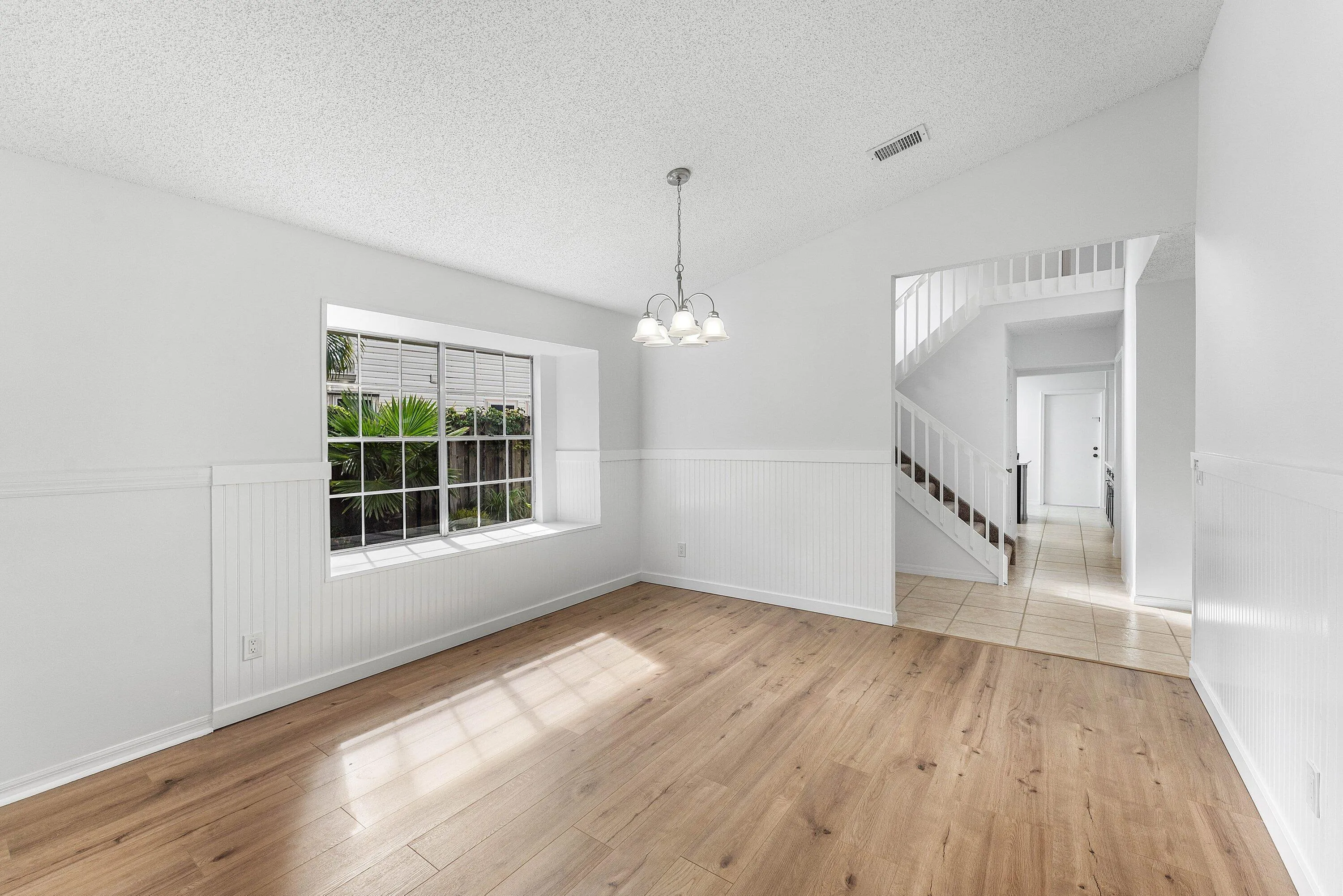 Spacious interior featuring wood-finish flooring, wainscoting details, a prominent window, and a vaulted ceiling