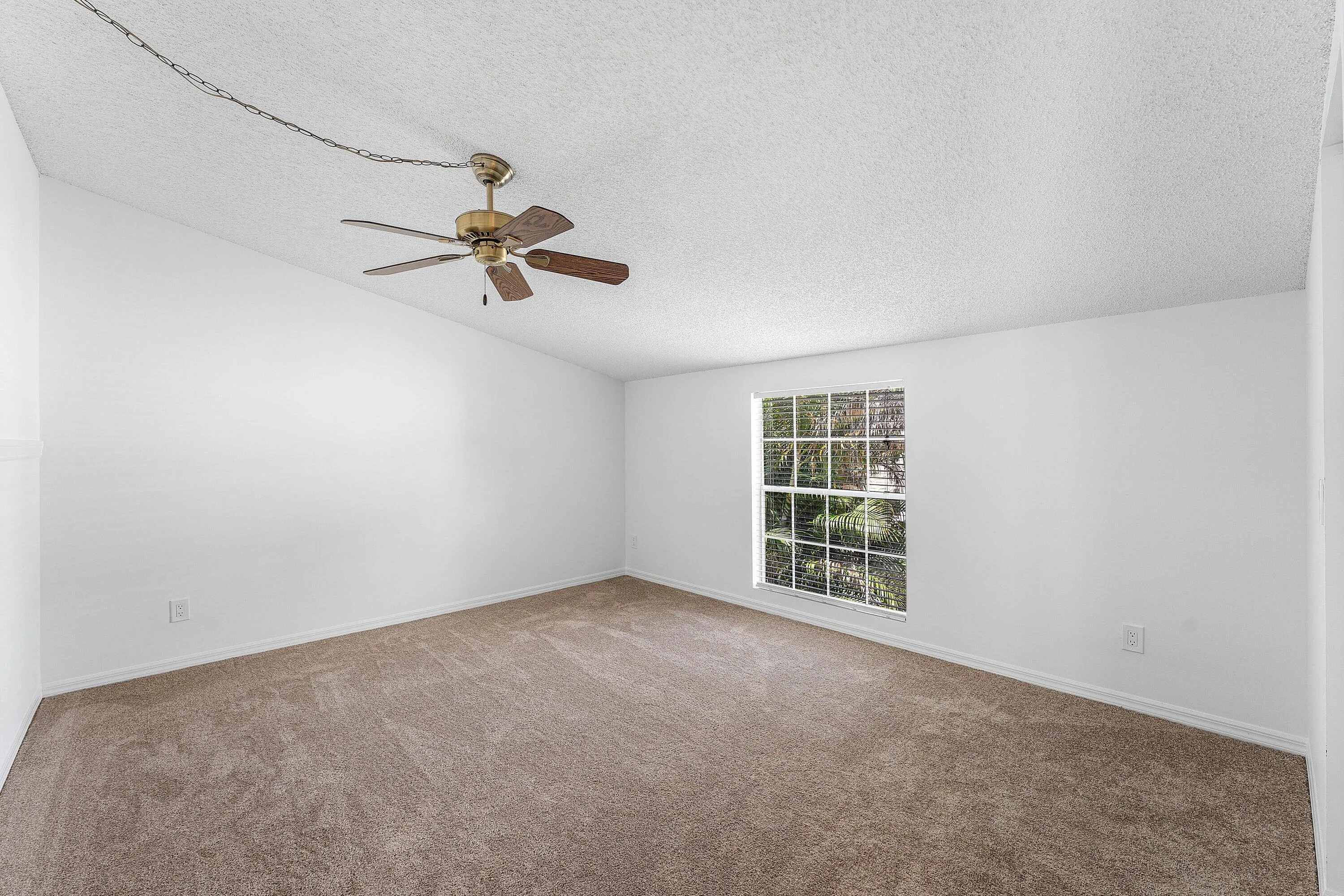 Spacious room featuring neutral carpeting, white painted walls, a textured ceiling, a window with exterior views, and a ceiling fan with integrated lighting