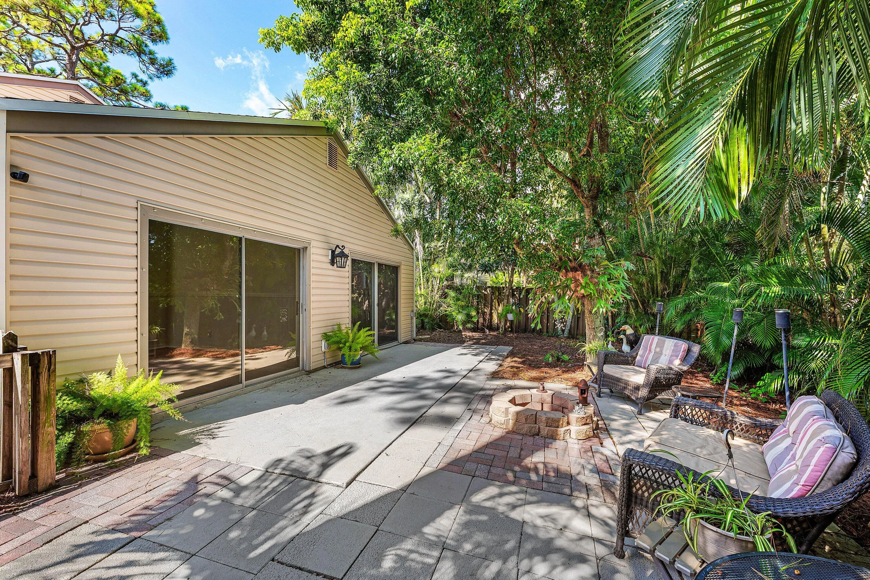 Expansive outdoor patio featuring a combination of paver and brick surfaces, surrounded by lush, mature tropical landscaping