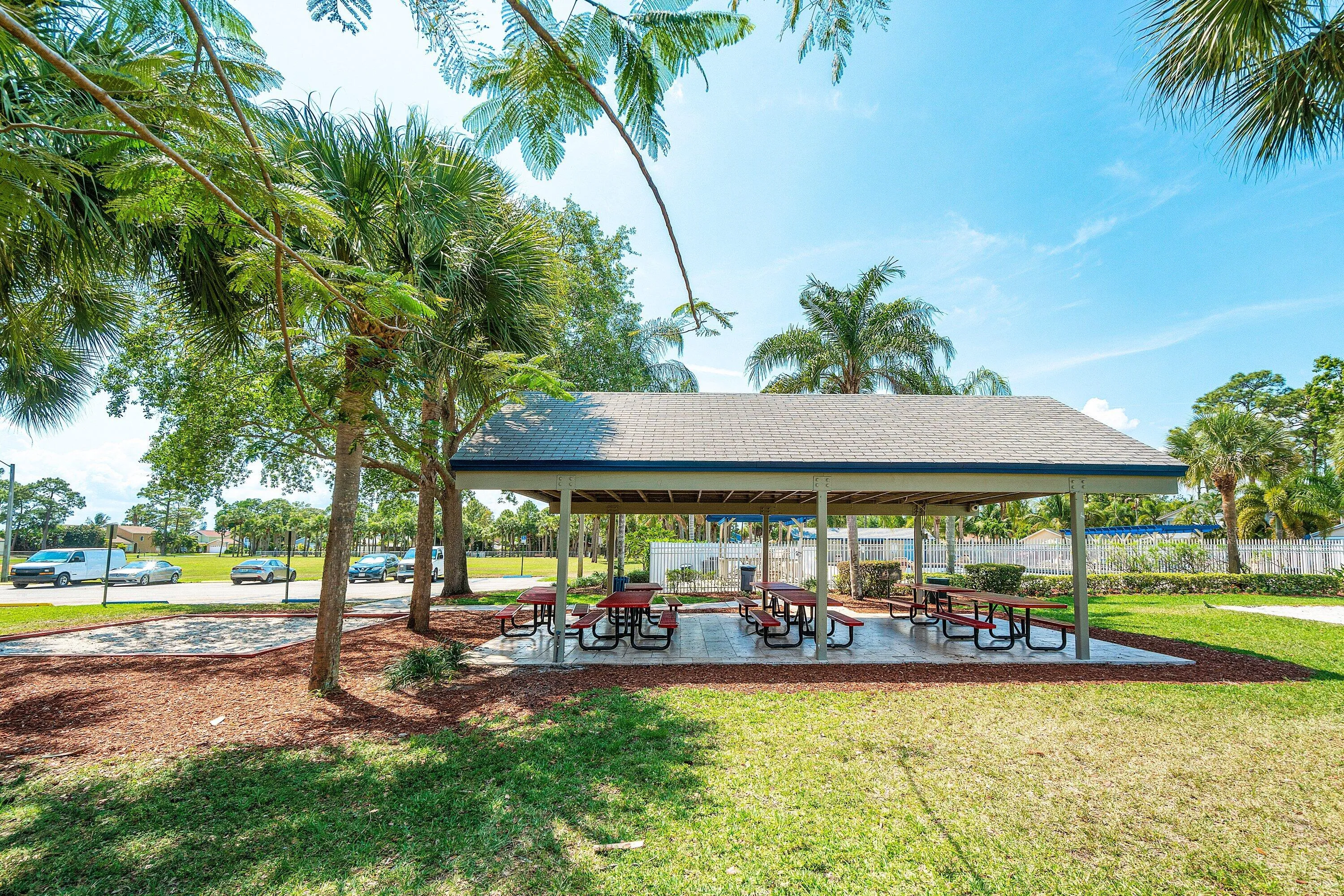 Covered outdoor pavilion with multiple picnic tables, surrounded by mature palm trees and green landscaping