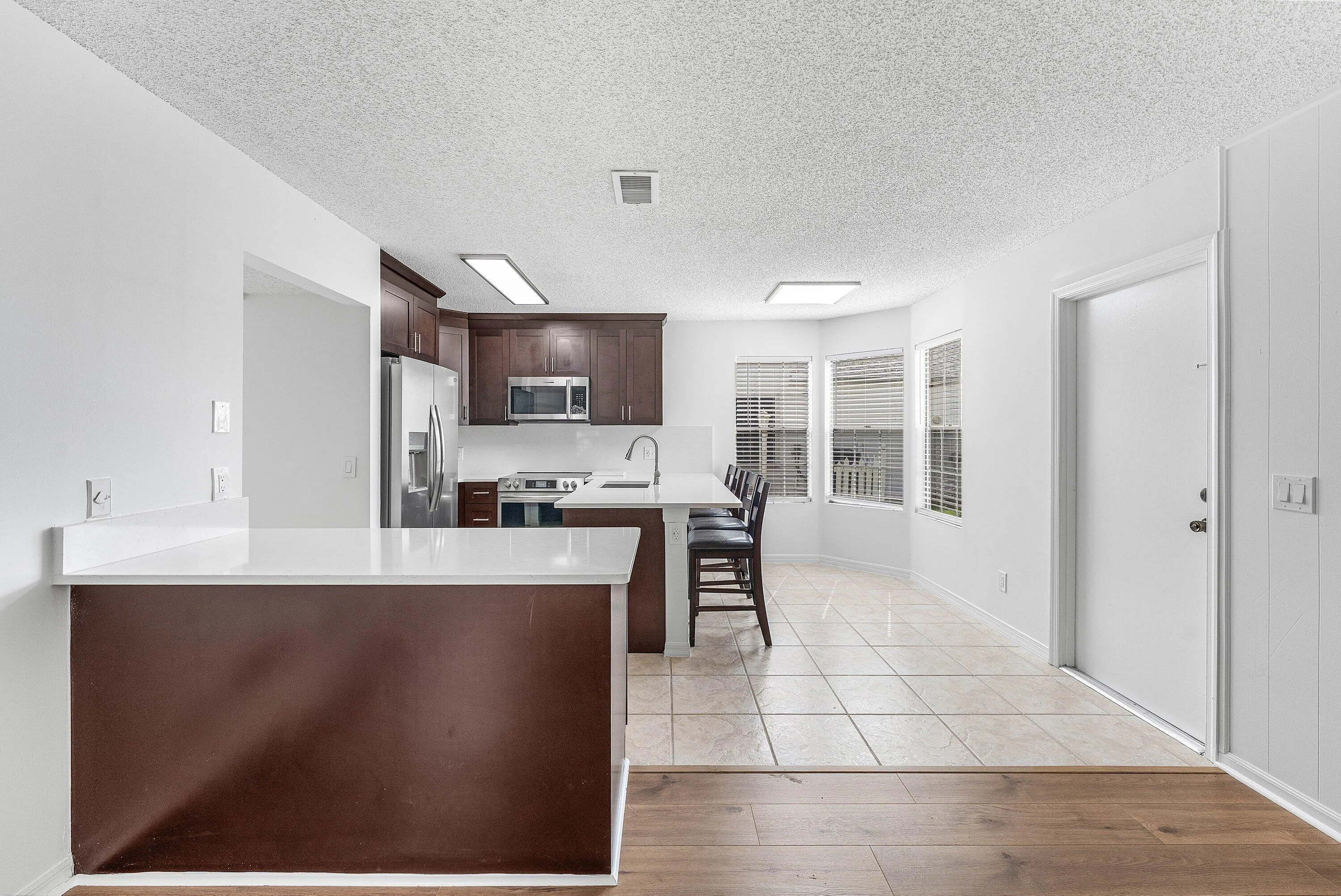 Kitchen featuring rich wood-finish cabinetry, stainless steel appliances, a white countertop island with seating, a tiled floor, and a bay window
