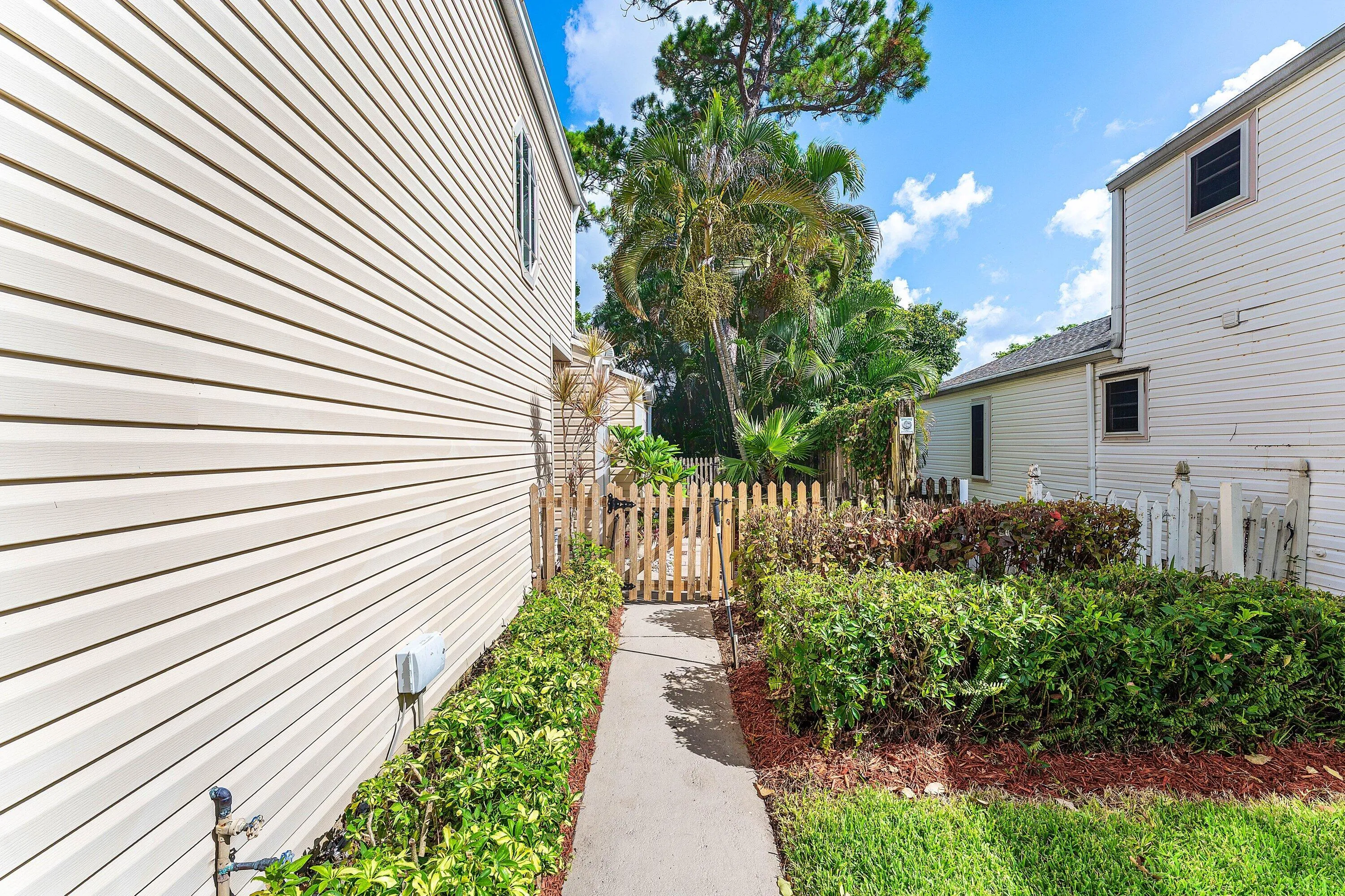 Exterior features include horizontal siding, a concrete pathway, a wooden picket fence, and established perimeter landscaping