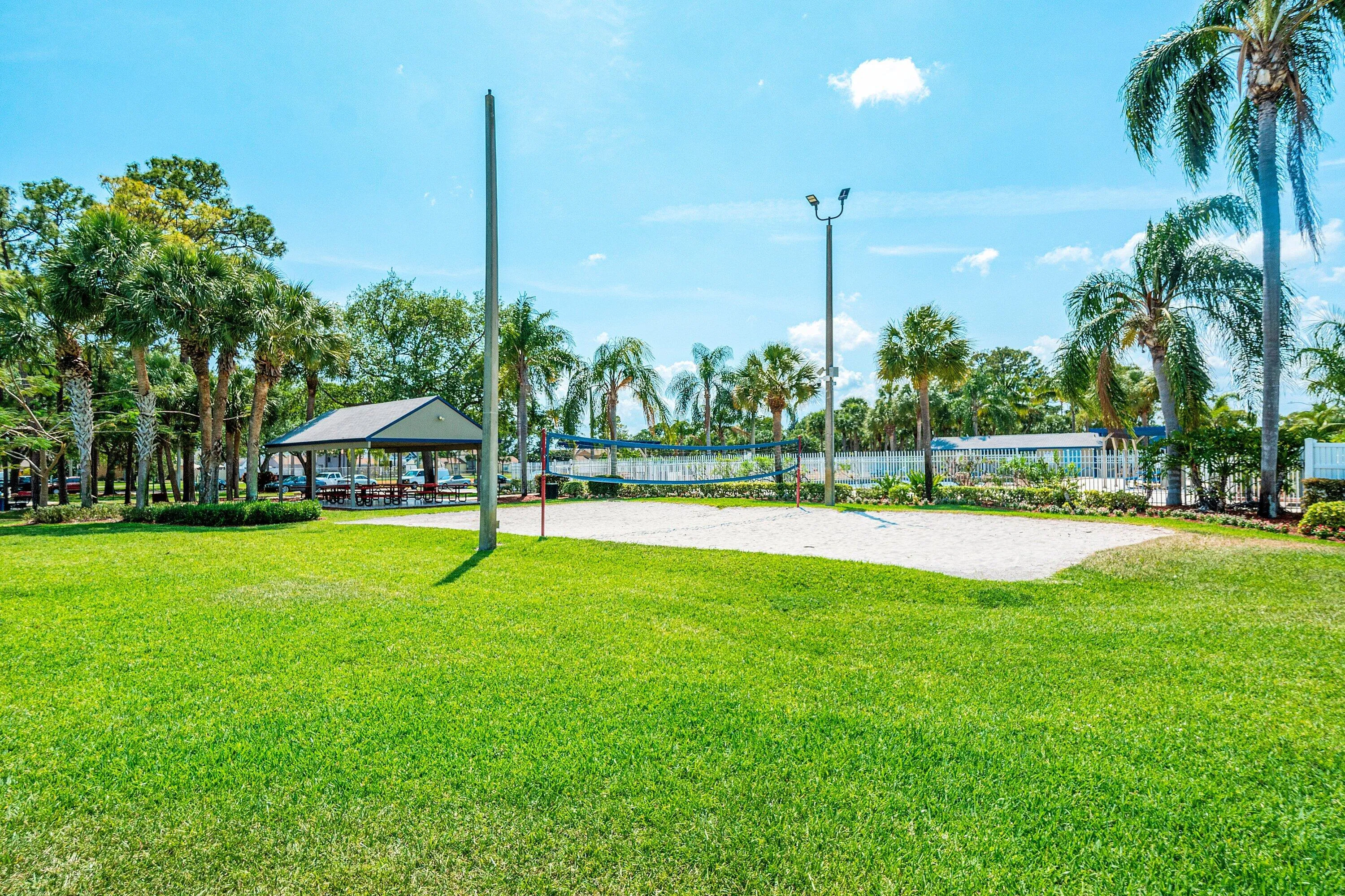 Sand volleyball court featuring a net and two poles, bordered by green lawn