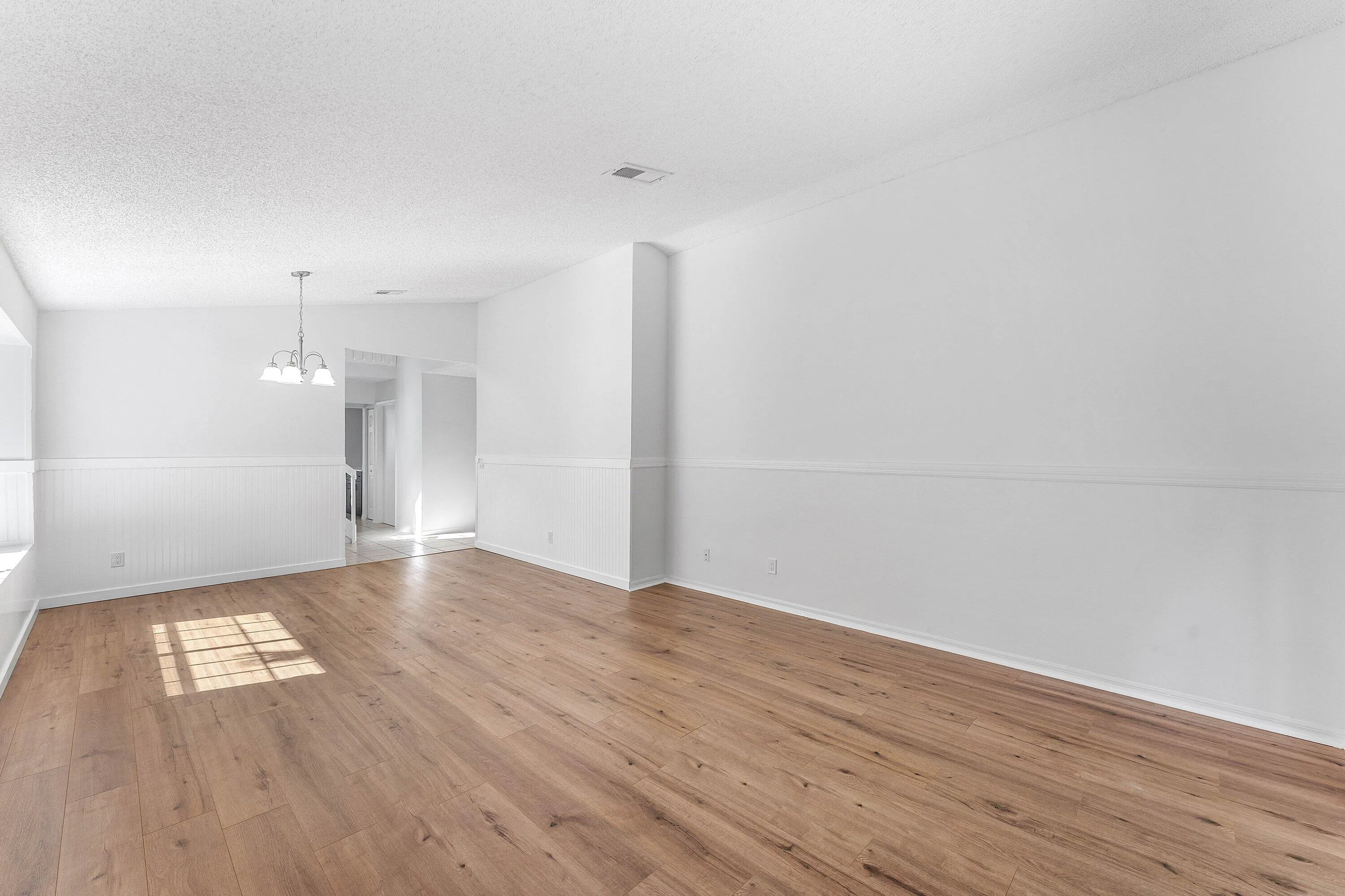 Spacious room featuring wood-finish flooring, white walls with wainscoting, and a ceiling-mounted light fixture