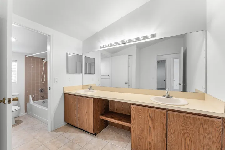 Double vanity with light wood-finish cabinetry, a single large mirror, and a linear vanity light fixture