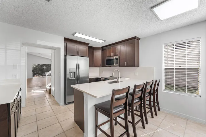 Kitchen featuring dark wood cabinetry, stainless steel appliances, a white solid surface countertop, and tile flooring