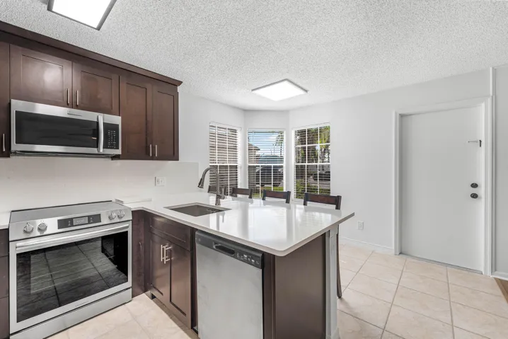 Modern kitchen featuring stainless steel appliances, dark wood-finish cabinetry, a light countertop, and tile flooring