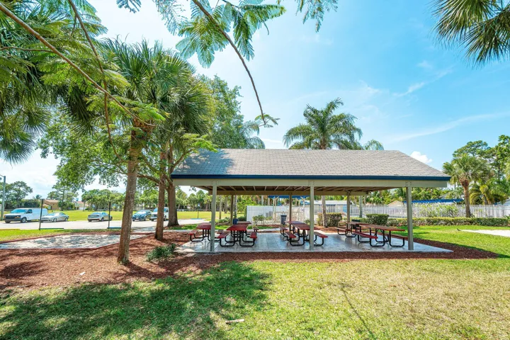Covered outdoor pavilion with multiple picnic tables, surrounded by mature palm trees and green landscaping