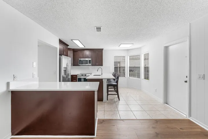 Kitchen featuring rich wood-finish cabinetry, stainless steel appliances, a white countertop island with seating, a tiled floor, and a bay window