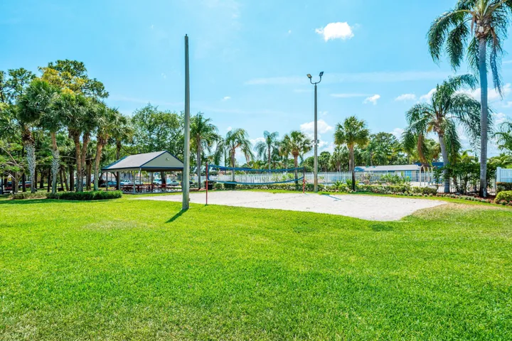 Sand volleyball court featuring a net and two poles, bordered by green lawn