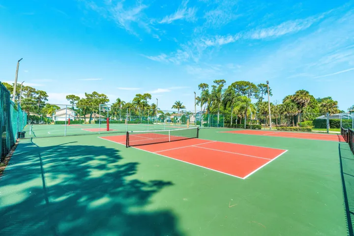 Multiple outdoor sports courts, including two tennis courts with red playing surfaces, a basketball court, and additional green court space