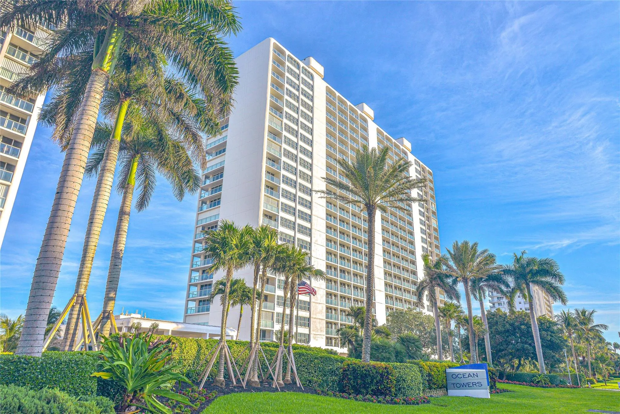 High-rise building with multiple balconies, surrounded by mature palm trees and manicured landscaping