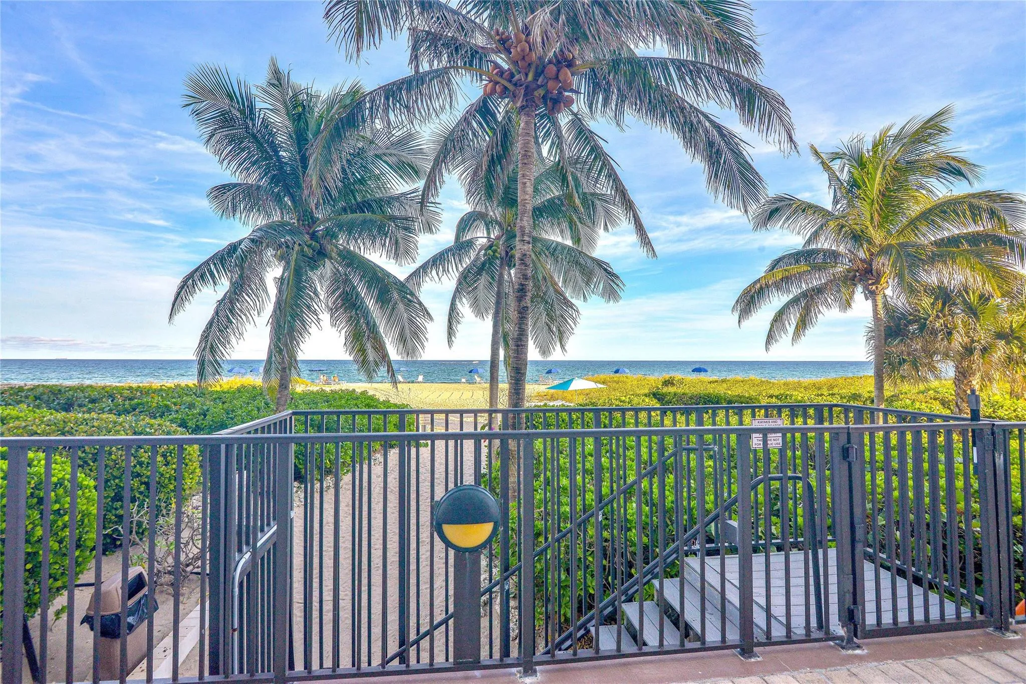 Direct beach access featuring a gated walkway, mature palm trees, and ocean backdrop