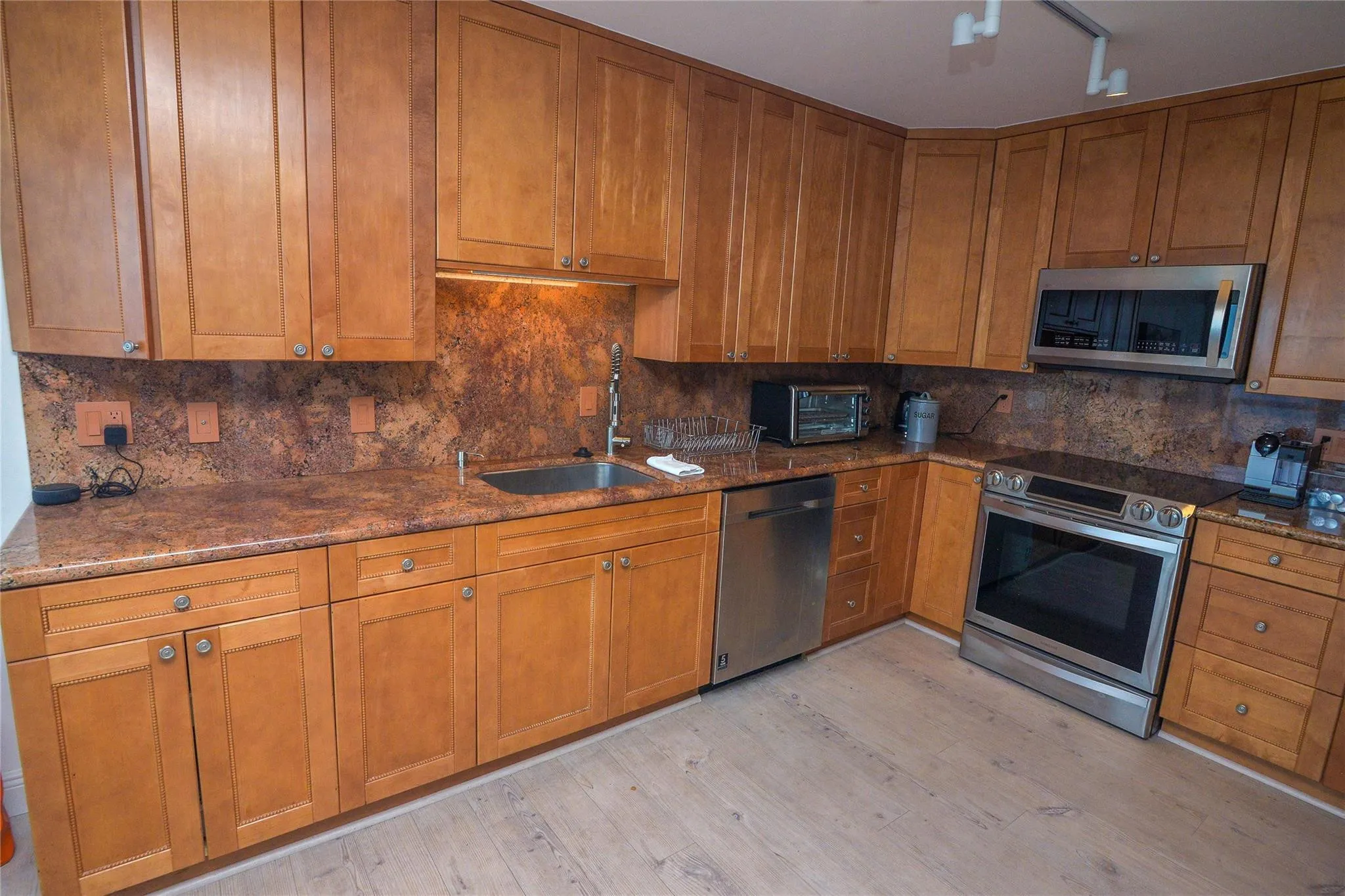 U-shaped kitchen featuring wood cabinetry, integrated stainless steel appliances, speckled countertops with coordinating backsplash, and wood-finish flooring