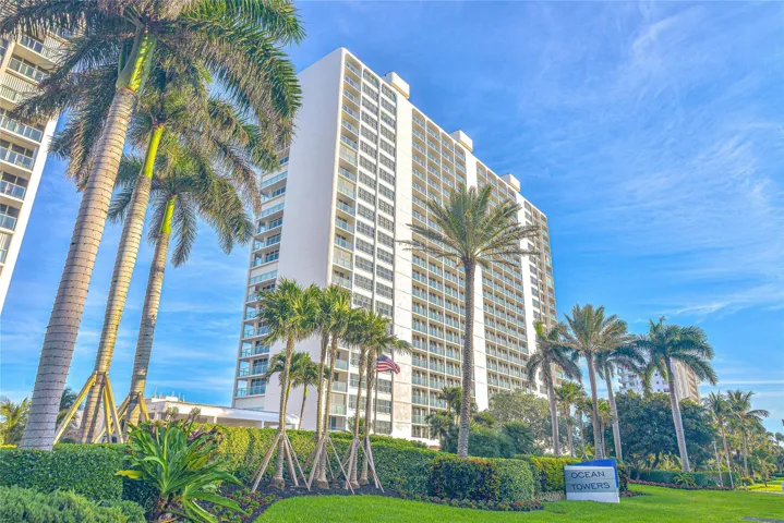 High-rise building with multiple balconies, surrounded by mature palm trees and manicured landscaping