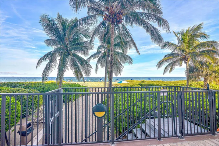 Direct beach access featuring a gated walkway, mature palm trees, and ocean backdrop