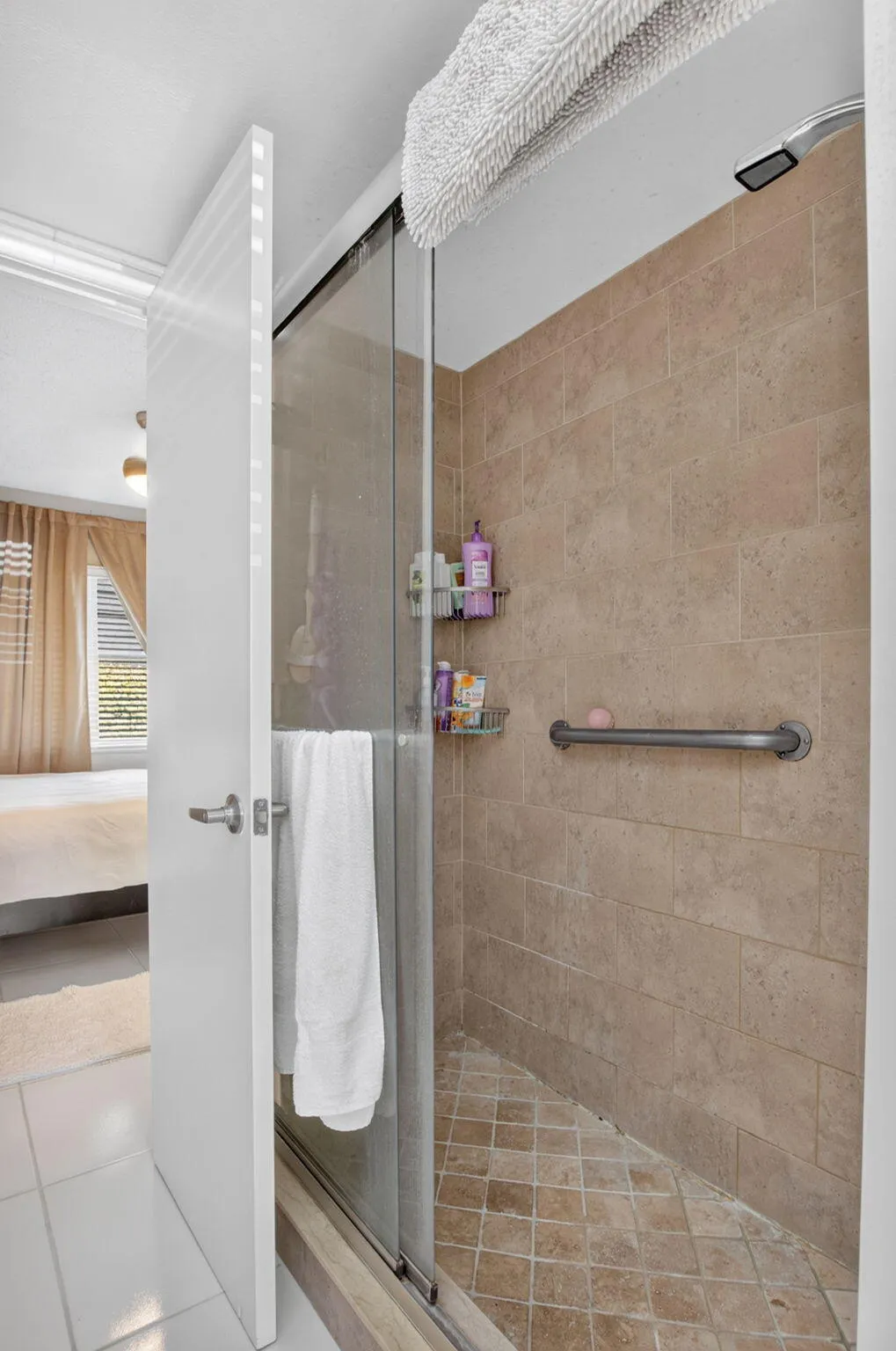 Walk-in shower featuring glass enclosure, large format tile walls, mosaic tile floor, and a mounted grab bar