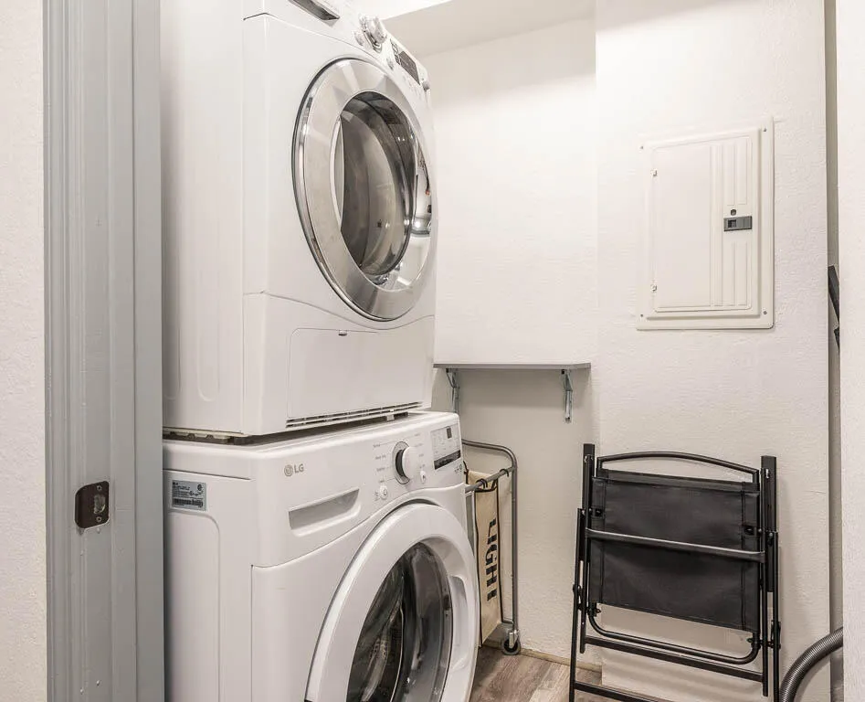 Dedicated laundry area featuring a stacked washer and dryer, wood-finish flooring, and a wall-mounted electrical panel