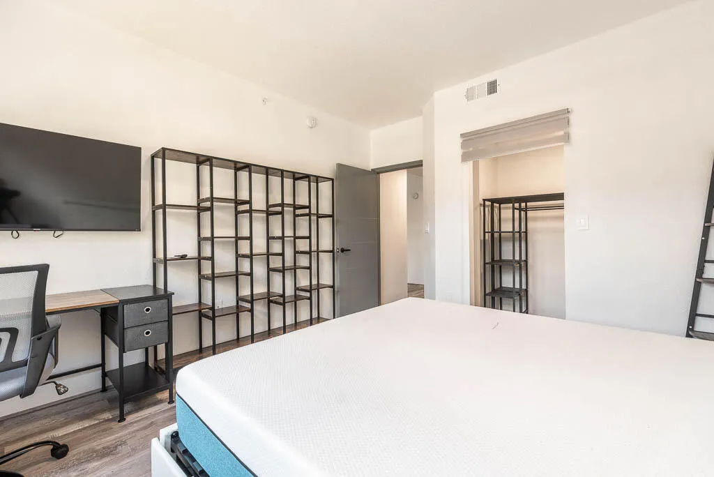 Bright room featuring wood-finish flooring, a built-in closet with shelving, and a wall-mounted shelving unit