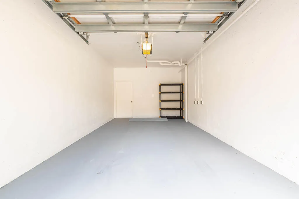 Spacious garage featuring a durable gray floor coating, white painted walls, exposed ceiling framing, and an overhead door opener mechanism